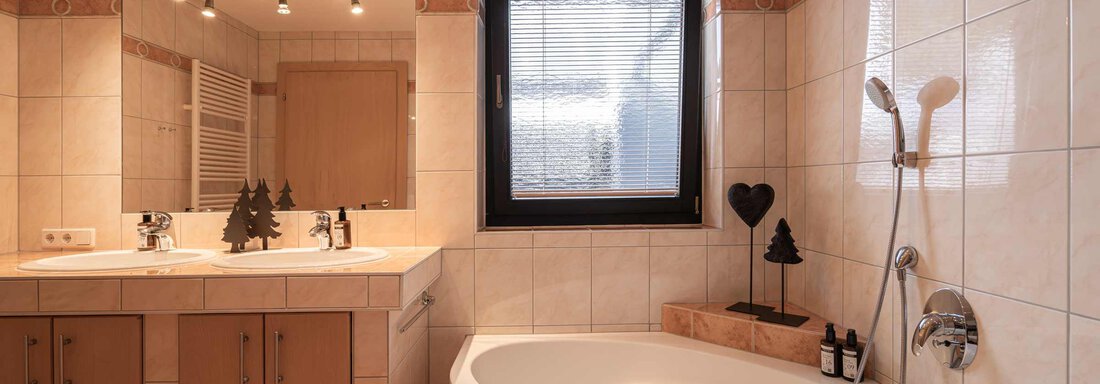 Ein modernes Badezimmer mit einer Badewanne, einem Waschbecken und einem großen Fenster. Die Wände sind mit hellen Fliesen gestaltet, und es sind dekorative Elemente vorhanden. - Apart Reinstadler - Sölden