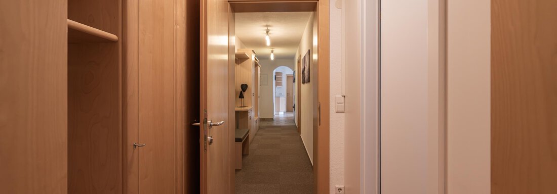 Ein schmaler Flur mit Holzregalen und mehreren Türen. Der Boden ist mit Teppich ausgelegt und es gibt eine helle Beleuchtung. - Apart Reinstadler - Sölden