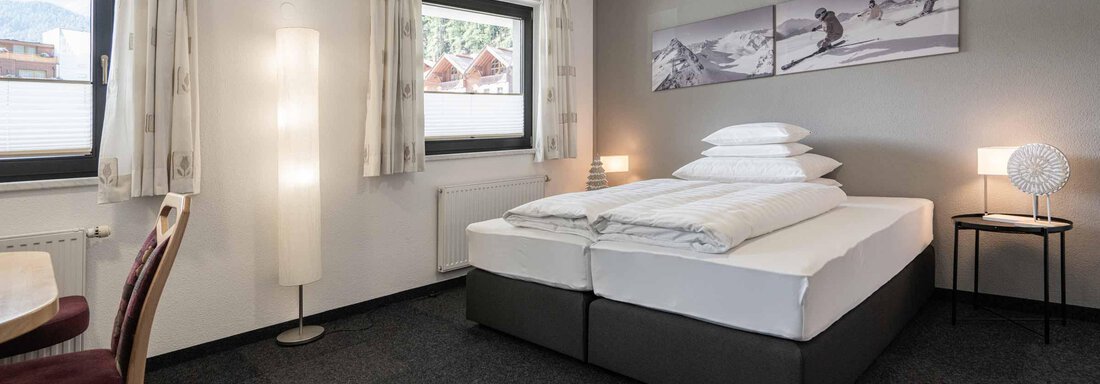 Ein gemütliches Schlafzimmer mit einem großen Bett und zwei Fenstern. Die Einrichtung ist modern und einladend, mit einem Tisch und Stühlen. - Apart Reinstadler - Sölden