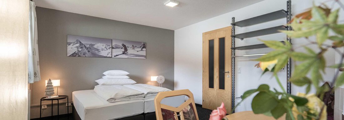 Ein modernes Zimmer mit einem Doppelbett, einem Tisch und Stühlen. An der Wand hängen Bilder von Schneelandschaften. - Apart Reinstadler - Sölden