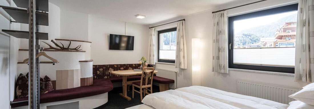 Ein gemütliches Zimmer mit zwei Betten, einem Tisch und einer Sitzecke. Große Fenster bieten Blick nach draußen und viel Tageslicht. - Apart Reinstadler - Sölden