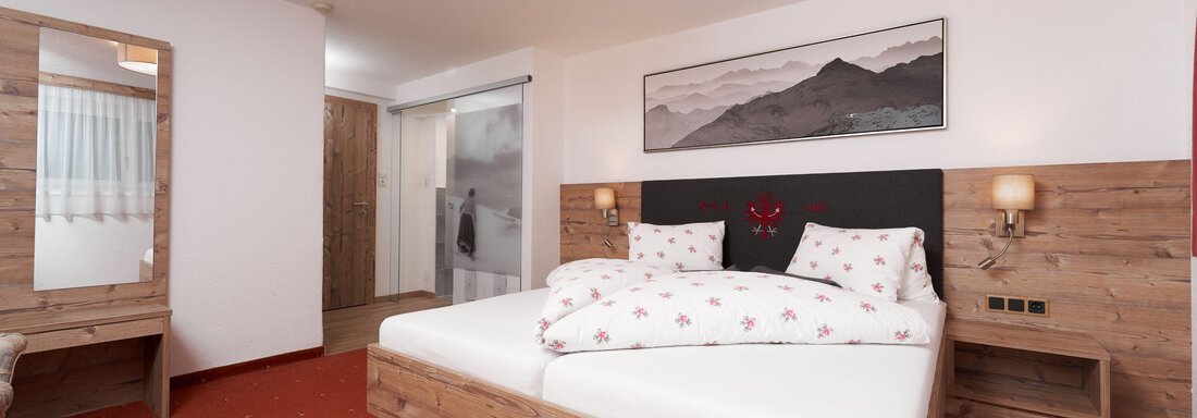 A modern bedroom with a cozy double bed and wooden furniture. The walls are light, and a picture of mountains hangs above the bed. - Apart Sunnhäusl - Sölden