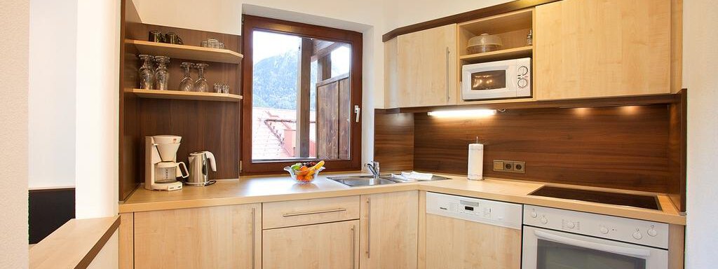 Eine moderne Küche mit hellen Holzschränken und einem Fenster, das auf die Berge blickt. Sie ist gut ausgestattet mit Geräten wie einem Kühlschrank, einem Herd und einer Mikrowelle. - Appartement Alpin - Sölden