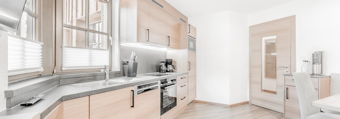 Eine moderne Küche mit holzfarbenen Schränken und einem hellen, einladenden Ambiente. Die Arbeitsfläche ist aus grauem Stein und es gibt eine separate Tür zum Nebenraum. - Appartement Montanara - Sölden