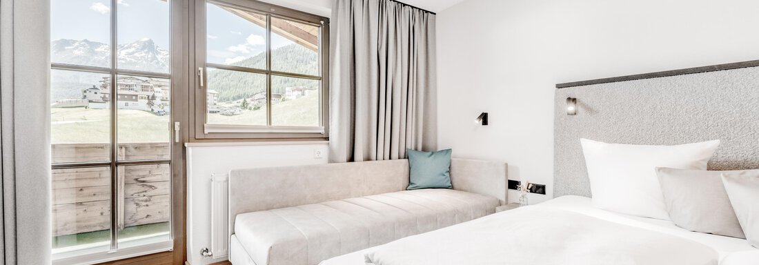 Ein modernes Hotelzimmer mit einem großen Fenster und Ausblick auf die Berge. Es gibt ein Doppelbett und eine gemütliche Sitzecke. - Appartement Montanara - Sölden