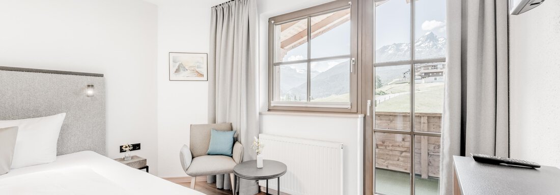Ein modernes Schlafzimmer mit einem großen Bett und hellen Vorhängen. Das Zimmer hat einen kleinen Tisch und einen schönen Ausblick auf den Balkon. - Appartement Montanara - Sölden
