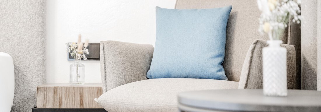 Ein gemütlicher Sessel mit einem blauen Kissen steht neben einem kleinen Tisch. Auf dem Tisch befindet sich eine Vase mit Blumen. - Appartement Montanara - Sölden