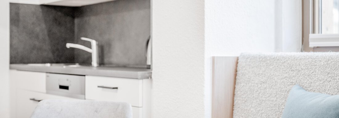 Eine moderne, minimalistische Küche mit hellen Schränken und einem großen Fenster. Der Tisch ist aus Holz und neben ihm befindet sich ein bequemer Sitzbereich. - Appartement Montanara - Sölden