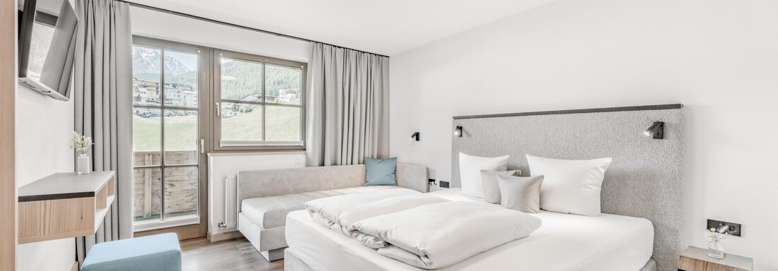 Ein modernes Hotelzimmer mit einem großen Doppelbett und einer komfortablen Sitzecke. Licht fällt durch die Fenster und schafft eine helle, einladende Atmosphäre. - Appartement Montanara - Sölden