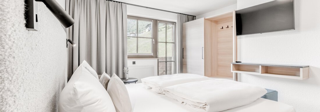 Ein modernes Schlafzimmer mit einem großen Bett und hellen Wänden. Es gibt einen Fernseher und ein Fenster, das viel Licht hereinscheinen lässt. - Appartement Montanara - Sölden