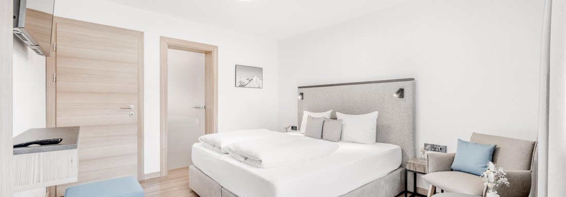Ein modernes Schlafzimmer mit einem großen Bett, einem Fernseher und einem kleinen Tisch. Der Raum hat einen hellen, einladenden Look mit Holzfußboden. - Appartement Montanara - Sölden