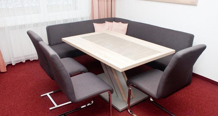 Ein moderner Essbereich mit einer quadratischen Holzwerktisch und gepolsterten Stühlen. Der Raum hat einen gemütlichen Teppich in Rot und helle Vorhänge. - Appartement Viertler - Sölden