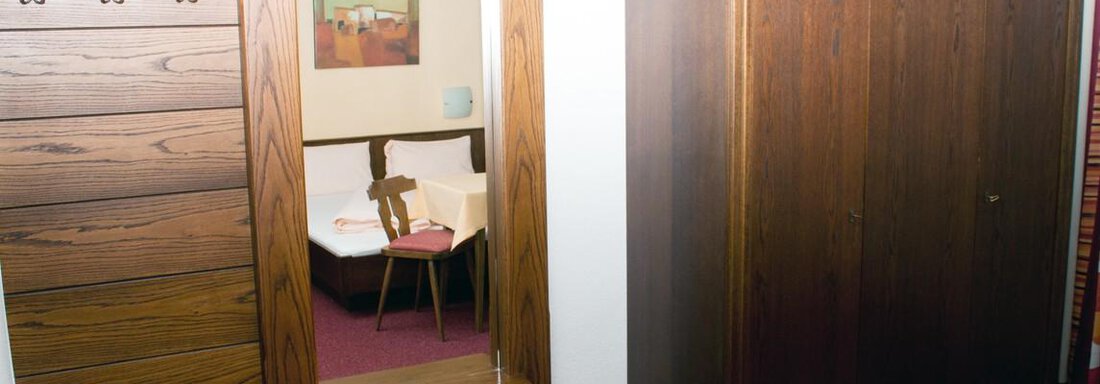 Ein einfacher Raum mit einem Holzschrank und einer Spiegelwand. Im Hintergrund ist eine gemütliche Sitzecke und ein Tisch zu sehen. - Appartement Viertler - Sölden