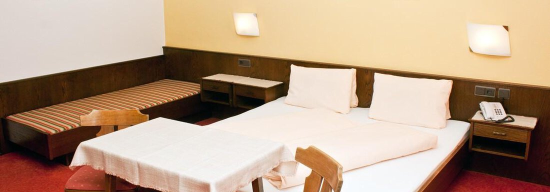Ein einfaches Hotelzimmer mit einem Doppelbett, einem Tisch und Stühlen. Die Wände sind in hellen Farben gehalten, und es gibt eine kleine Sitzecke. - Appartement Viertler - Sölden