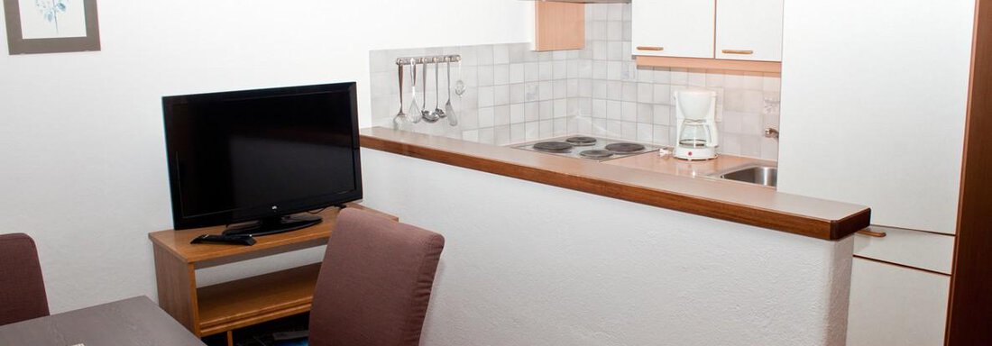 Ein gemütliches Wohnzimmer mit einem Esstisch, einem Fernseher und einer offenen Küchenecke. Die Einrichtung ist einfach und modern gestaltet. - Appartement Viertler - Sölden