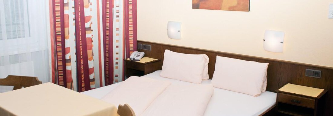 Ein einfaches Zimmer mit einem Doppelbett und einem kleinen Tisch. Die Wände sind hell gestrichen und es gibt vorhänge mit bunten Mustern. - Appartement Viertler - Sölden