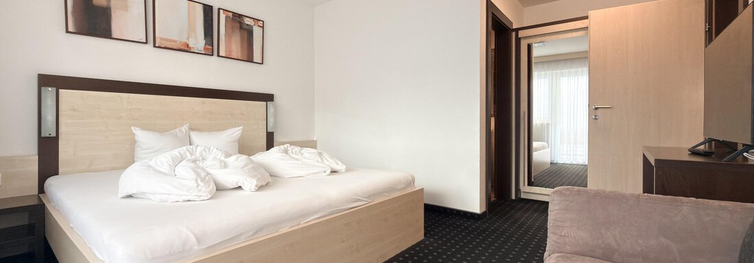 A modern room with a double bed and a comfortable sofa. The walls are painted light and decorated with pictures. - Appartementhaus A CASA "Kristall" - Sölden