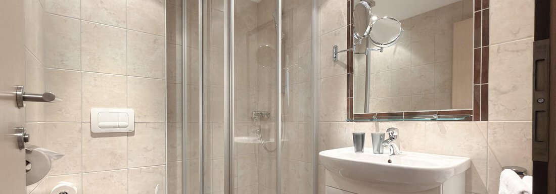 A modern bathroom with a glass shower and a sink. The walls are tiled with light tiles and there is a toilet. - Appartementhaus A CASA "Kristall" - Sölden