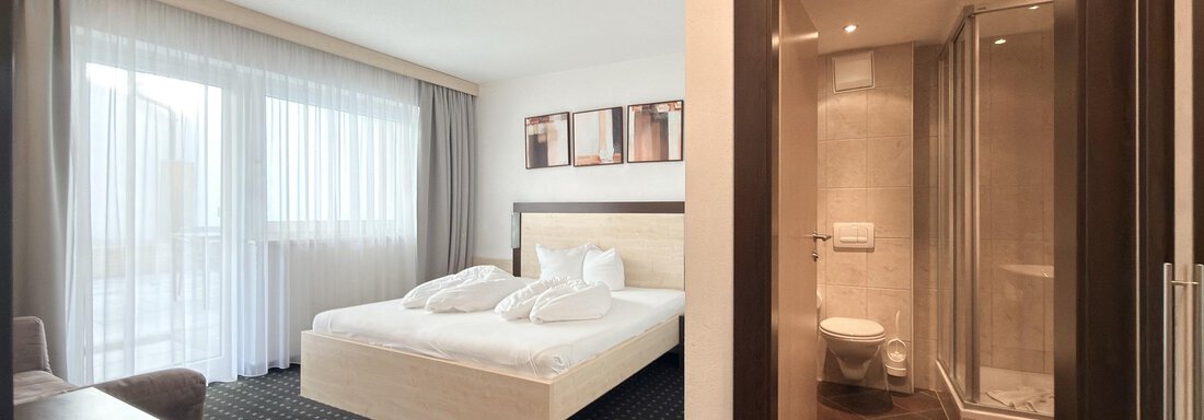 A modern hotel room with a double bed and large windows. The bathroom is separated by a door and well-equipped. - Appartementhaus A CASA "Kristall" - Sölden