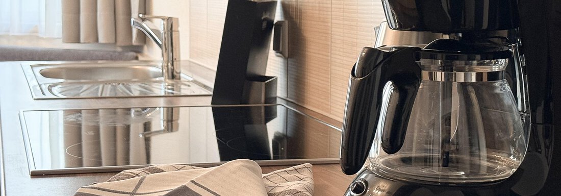 A modern kitchen with a black coffee machine on a wooden countertop. In the background, a sink and a cooktop are visible. - Appartementhaus A CASA "Kristall" - Sölden