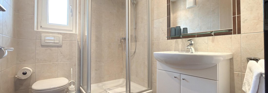 A modern bathroom with a shower, sink, and toilet. The walls are designed with bright tiles and brown floor tiles. - Appartementhaus A CASA "Kristall" - Sölden