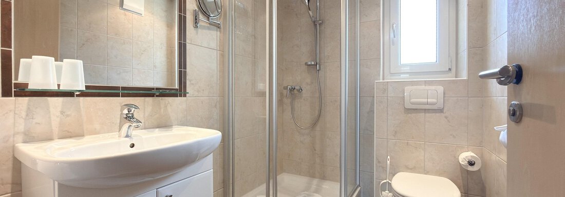 A modern bathroom with a shower cabin and a sink. The walls are brightly tiled, and there is a window that lets in natural light. - Appartementhaus A CASA "Kristall" - Sölden