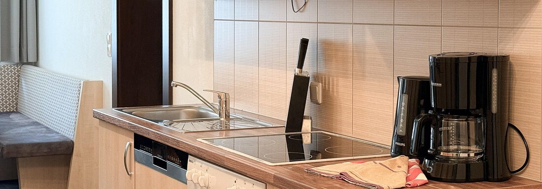 A modern kitchen with wooden cabinets and silver appliances. The equipment includes a stove, a sink, and a coffee maker. - Appartementhaus A CASA "Kristall" - Sölden