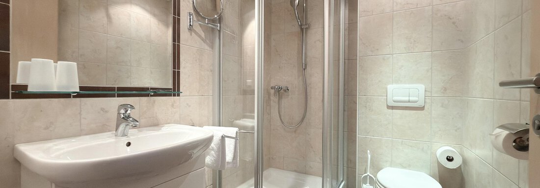 A modern bathroom with a shower and a washbasin. The walls are tiled in light colors, and the furnishings are simple and elegant. - Appartementhaus A CASA "Kristall" - Sölden