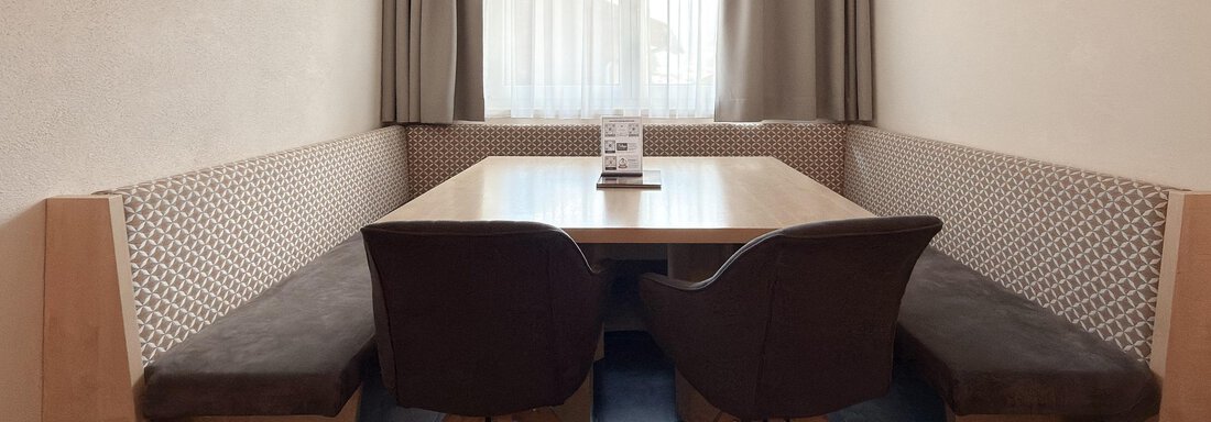 A cozy dining area with a wooden-clad bench and two chairs. The room is bright and cheerful, with a large window and curtains. - Appartementhaus A CASA "Kristall" - Sölden
