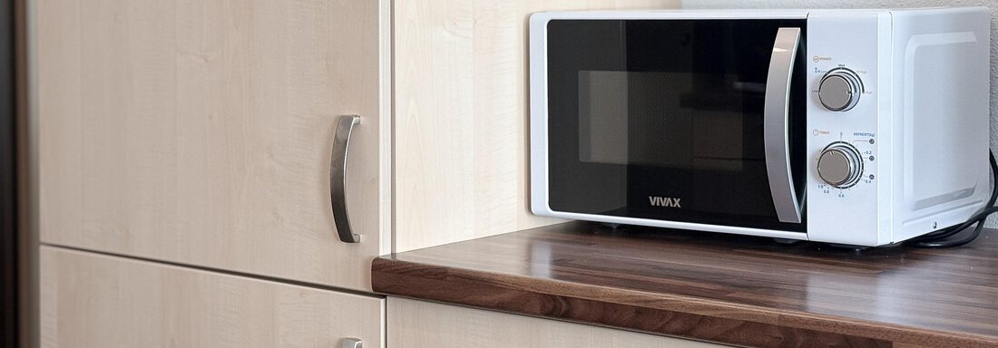 A modern microwave is on a wooden countertop. The background consists of light cabinets with smooth surfaces. - Appartementhaus A CASA "Kristall" - Sölden