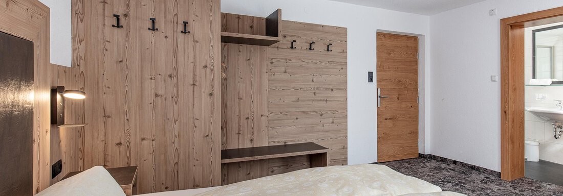 A cozy room with two beds, red pillows, and a television. The walls are in warm wood and red tones. - Appartementhaus Fender - Sölden