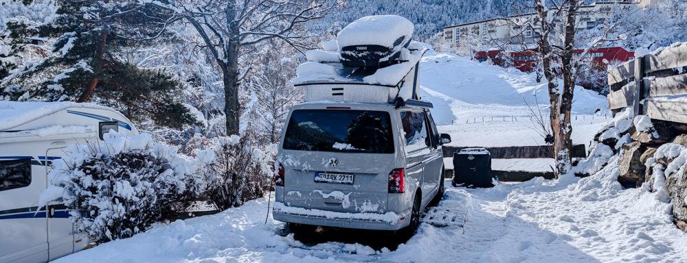 Stellplatz Panorama Winter A car is standing in the snow, surrounded by a winter landscape. In the background, snow-covered mountains and a clear sky can be seen. - Camping Sölden - Sölden