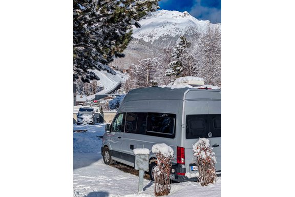 A motorhome is parked on a snow-covered parking lot with mountains in the background. The surroundings are wintry and picturesque. - Camping Sölden - Sölden