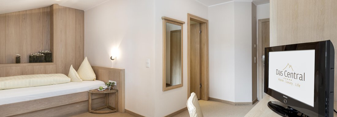253_DasCentral_byRudiWyhlidal-4558-edit Ein helles Zimmer mit modernem Interieur, einem Bett und einem Schreibtisch. Eine große Spiegelfläche und ein Fernseher sind ebenfalls vorhanden. - Das Central - Alpine . Luxury . Life - Sölden