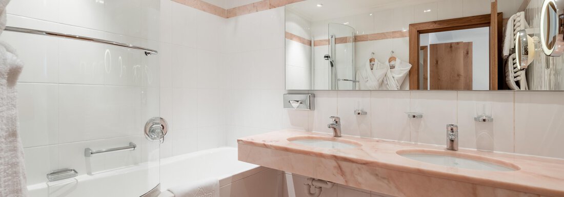 Ein modernes Badezimmer mit einer Badewanne und einem Doppelwaschbecken. Es gibt helle Wände und viel Licht durch die Deckenbeleuchtung. - Das Central - Alpine . Luxury . Life - Sölden