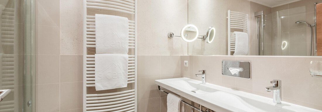 Ein modernes Badezimmer mit zwei Waschbecken und großen Spiegeln. Handtücher hängen an einem Heizkörper und die Beleuchtung sorgt für eine angenehme Atmosphäre. - Das Central - Alpine . Luxury . Life - Sölden