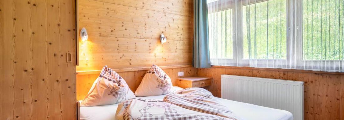 Ein gemütliches Schlafzimmer mit Holzverkleidung und einem großen Bett. Große Fenster sorgen für viel Tageslicht und Blick auf die grüne Landschaft. - Garni Nadine - Sölden
