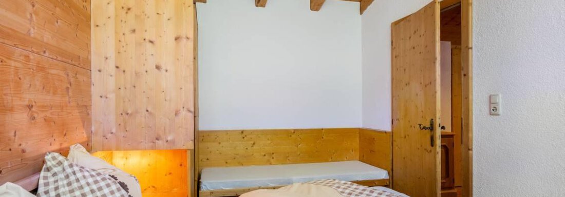 Ein gemütliches Schlafzimmer mit holzverkleideten Wänden und einem warmen Ambiente. Die Bettwäsche ist hell und sorgt für eine einladende Atmosphäre. - Garni Nadine - Sölden