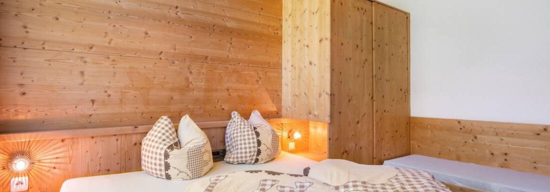 Ein gemütliches Schlafzimmer mit Holzwänden und einem großen Bett. Dekorative Kissen und sanfte Beleuchtung sorgen für eine warme Atmosphäre. - Garni Nadine - Sölden