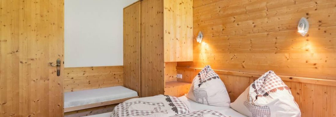 Ein gemütliches Schlafzimmer mit Holzwänden und einem Doppelbett. Es gibt einen Kleiderschrank und eine kleine Sitzecke. - Garni Nadine - Sölden