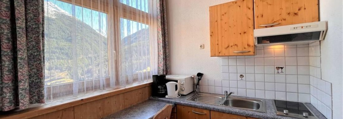 Eine helle Küche mit Holzschränken und modernen Geräten. Große Fenster bieten einen Blick auf die Berge. - Garni Nadine - Sölden