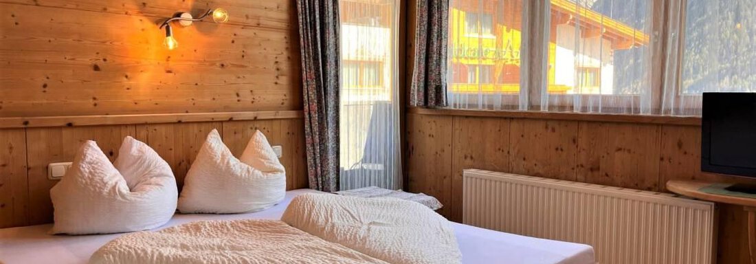 Ein gemütliches Zimmer mit Holzwänden und einem großen Bett. Es gibt weiche Kissen, großes Fenster und einen Fernseher. - Garni Nadine - Sölden