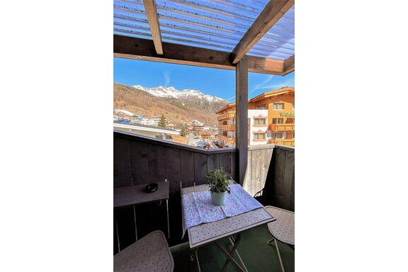 Ein gemütlicher Balkon mit einem Tisch und zwei Stühlen. Im Hintergrund sind die schneebedeckten Berge und eine schöne Aussicht auf die Stadt zu sehen. - Garni Nadine - Sölden