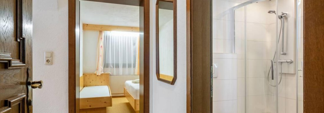 Ein heller Flur mit Holzfußboden und Türen zu einem Schlafzimmer und einem Badezimmer. Das Badezimmer ist modern gestaltet mit einer Dusche und einer hellen, freundlichen Atmosphäre. - Garni Nadine - Sölden