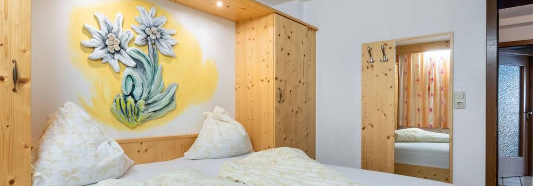 Ein gemütliches Schlafzimmer mit einem Doppelbett und Holzregalen. An der Wand hängt ein schönes Bild von Blumen. - Garni Nadine - Sölden