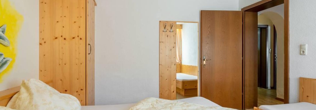 Ein gemütliches Schlafzimmer mit Holzverkleidungen und warmem Licht. Es gibt zwei Betten und eine offene Tür, die zu einem weiteren Raum führt. - Garni Nadine - Sölden