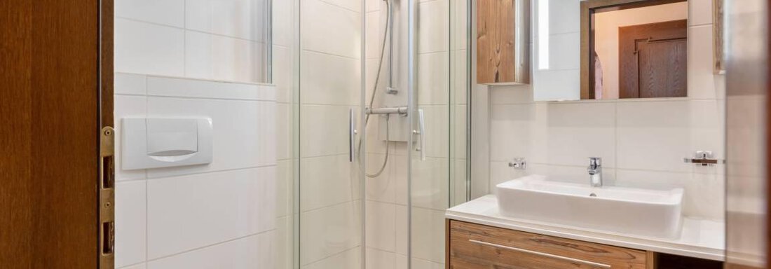 Ein modernes Badezimmer mit einer runden Dusche und einem eleganten Waschbecken. Die Wände sind mit weißen Fliesen und Holzverkleidungen gestaltet. - Garni Nadine - Sölden