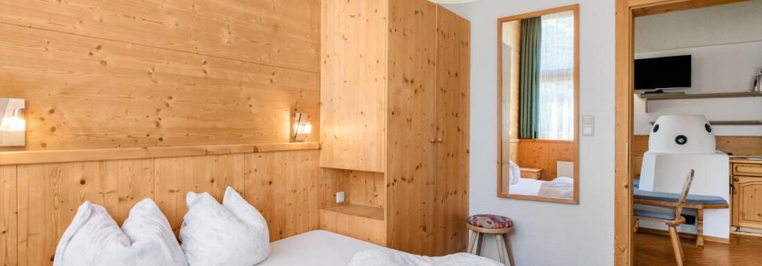 Ein gemütliches Schlafzimmer mit Holzverkleidung und einem großen Bett. Der Raum ist hell und einladend, mit einem kleinen Tisch und einem Spiegel. - Garni Nadine - Sölden