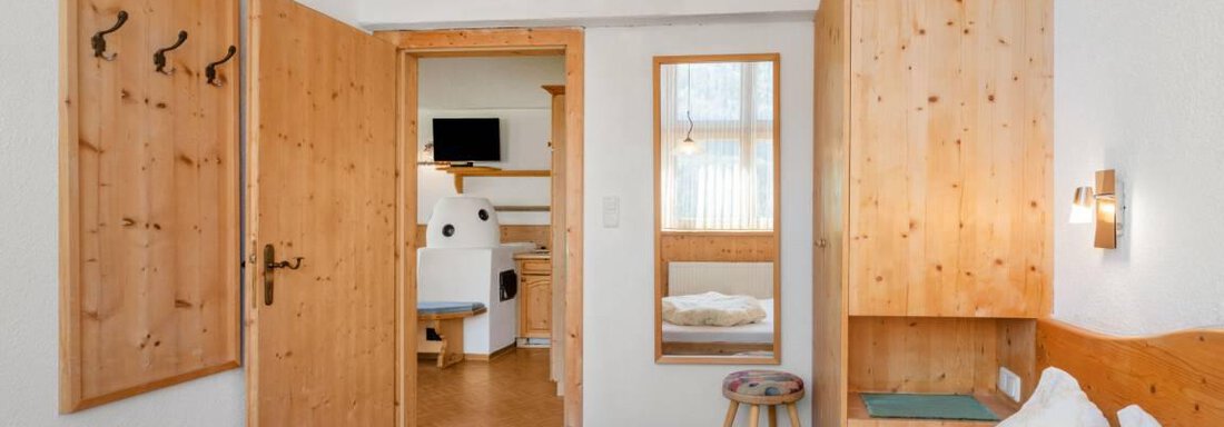 Ein gemütliches Schlafzimmer mit Holzverkleidung und einem großen Bett. Die Tür führt zu einem hellen Badezimmer. - Garni Nadine - Sölden