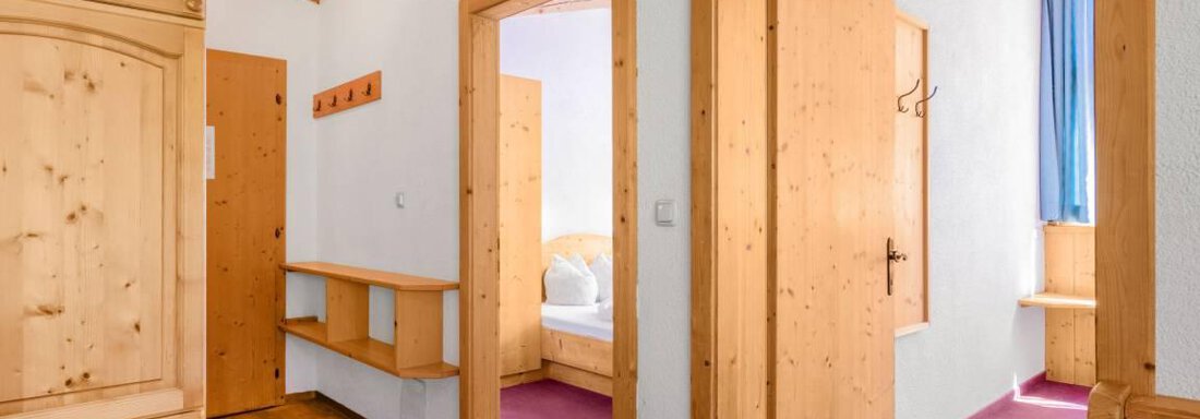 Ein gemütlicher Flur mit Holzmöbeln und zwei offenen Türen. Der Boden ist aus Holz und der Teppich ist pink. - Garni Nadine - Sölden